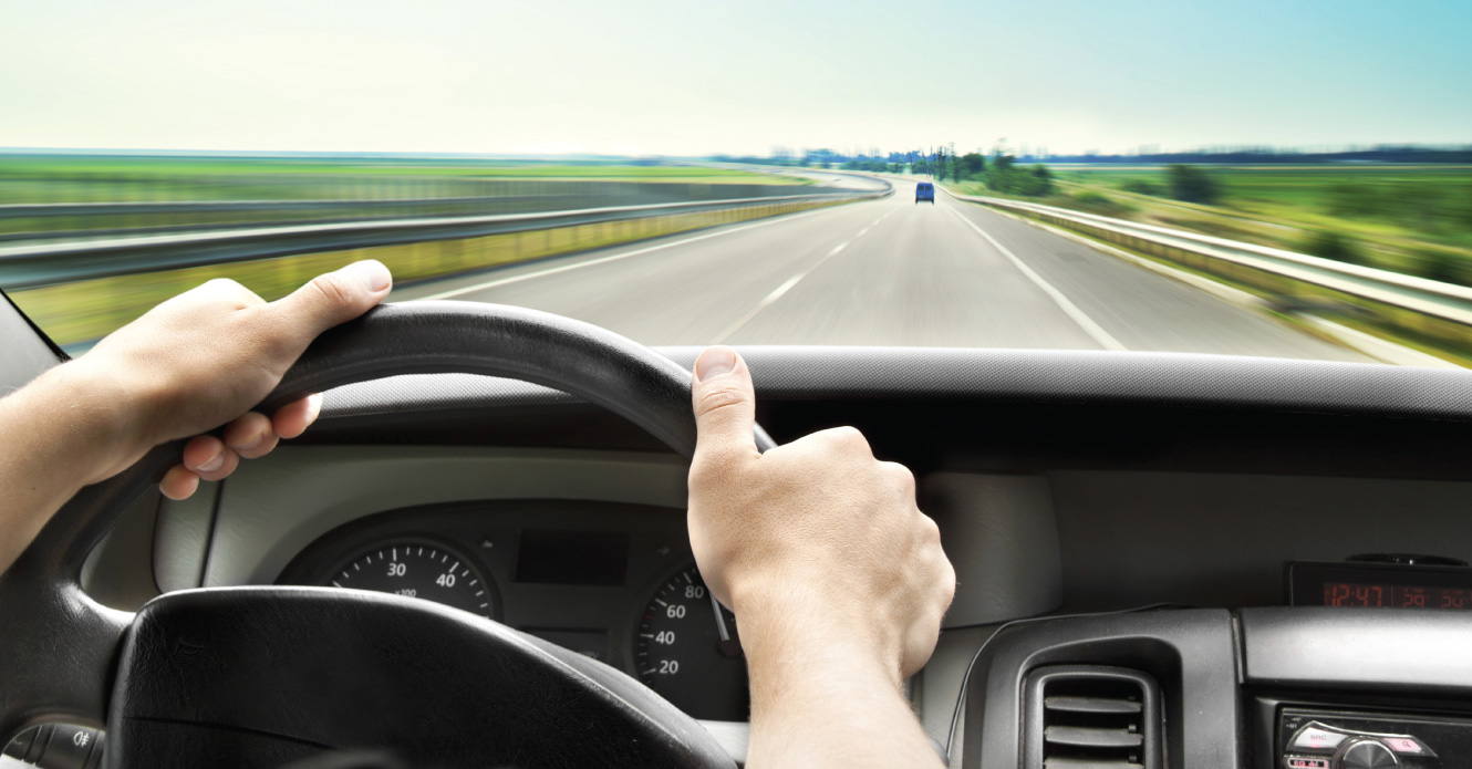 A man in a vehicle with hands on the steering wheel.