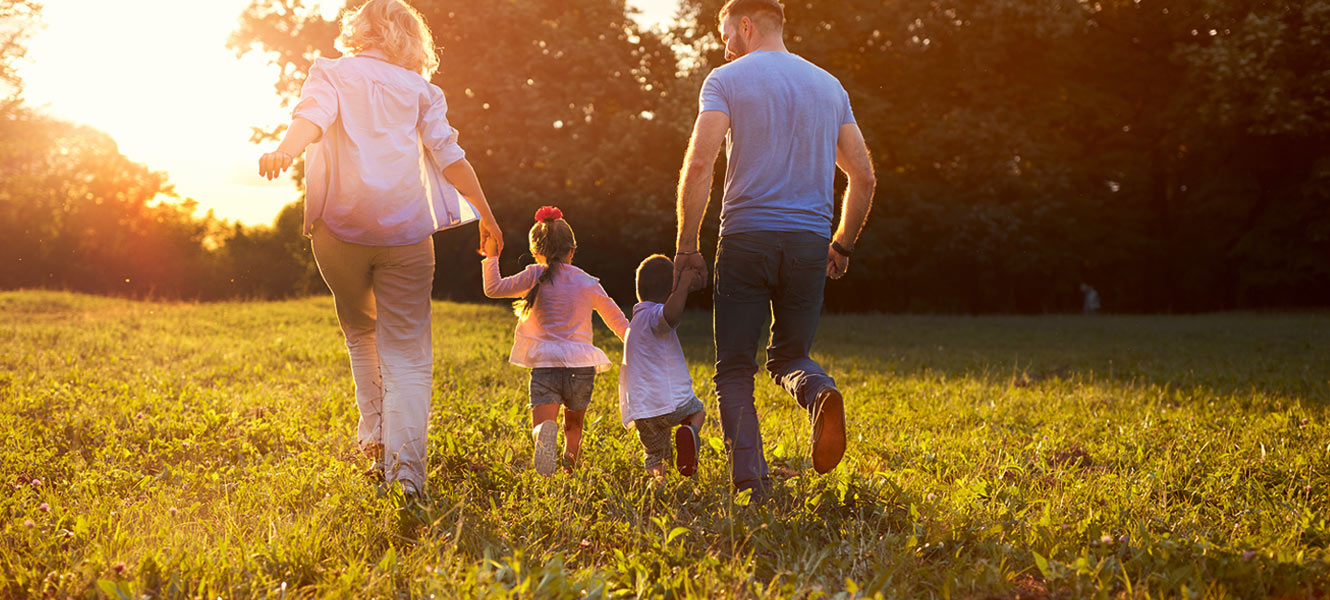 Family of four running through green grass in the sunshine